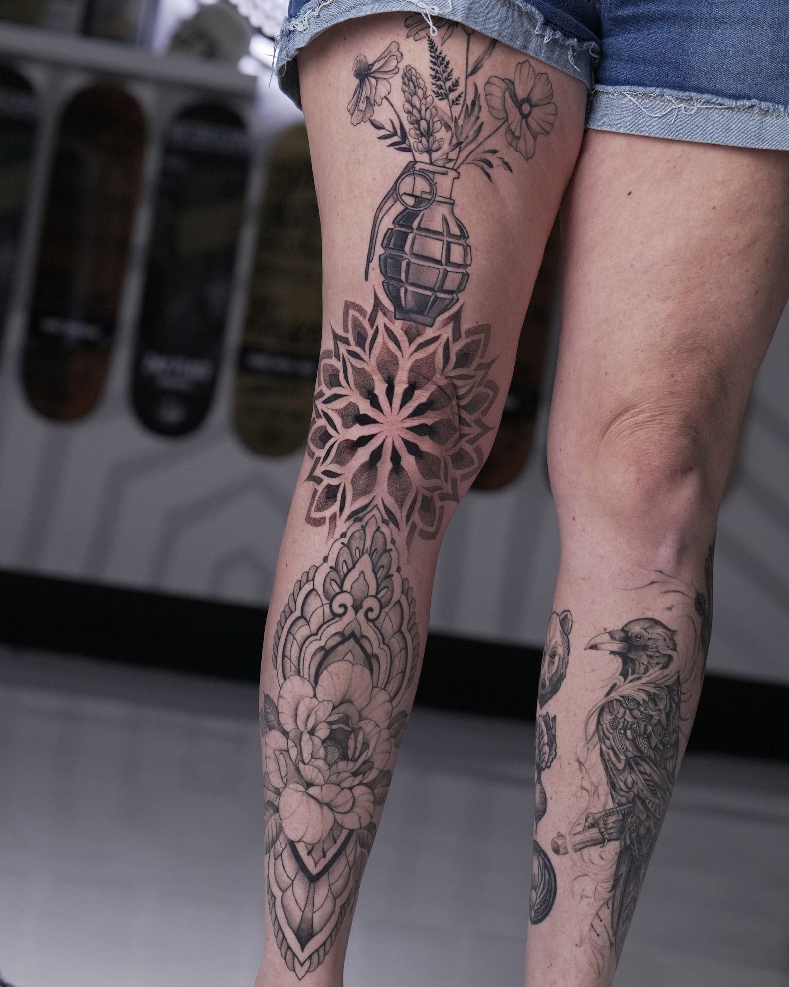 Ornamental black and grey leg tattoo — flowers blooming from a grenade above a geometric mandala