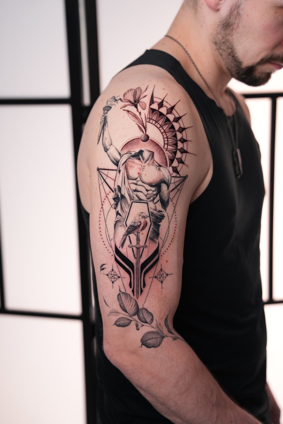 Black and grey half sleeve — heroic Greek mythological figure raising a torch above a sacred geometry mandala, with a sword and fine line florals